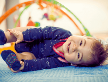 bebê sorridente sobre um tapete tatame na fase de quando o bebê começa a rolar