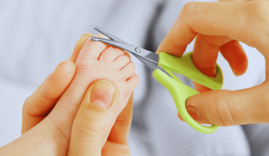 mãos cortando as unhas do pé de um bebê com uma tesourinha